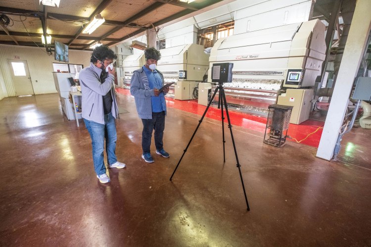 Two people standing near video tripod recording a virtual scan inside the cotton gin.